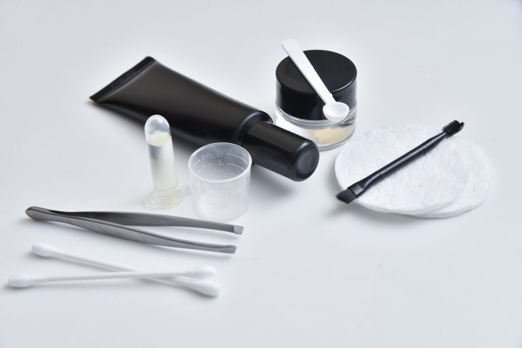 Professionelles Zubehör zum Augenbrauen färben - Pinzetten, Färbemittel, Bürstchen und Applikatoren auf weißer Unterlage