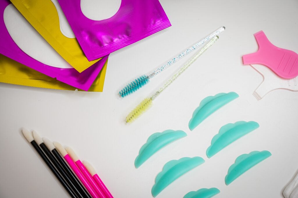 Ein Set für ein Wimpernlifting mit Silikonpads, Wimpernbürstchen und den Lotionen in bunten Sachets liegt auf einem Tisch.