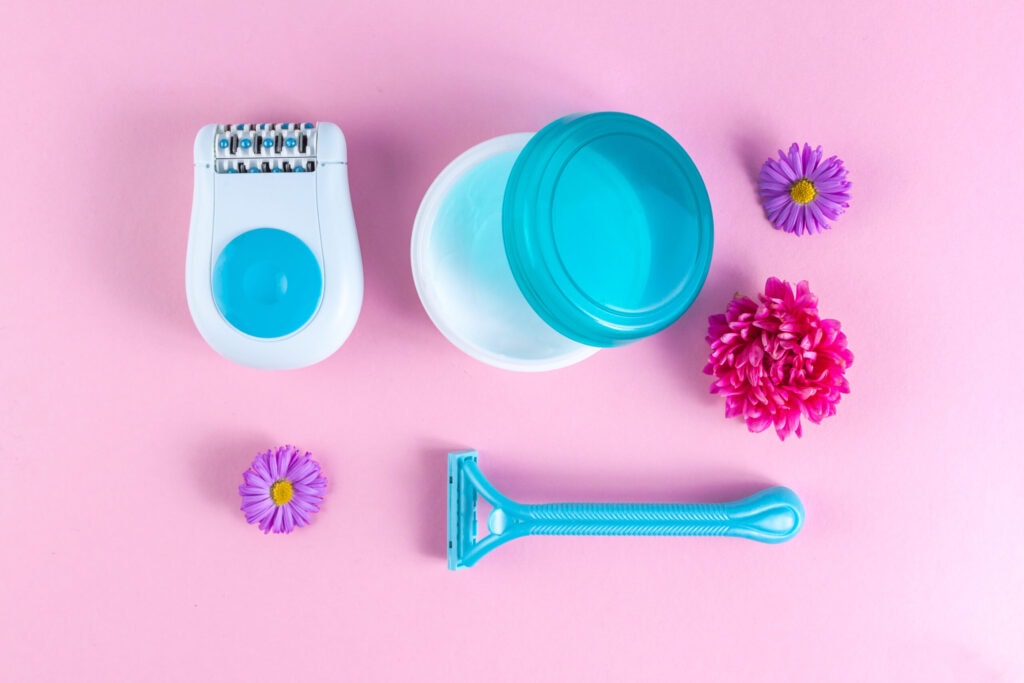 Ein Flat Lay mit sanften Produkten für die Haarentfernung im Intimbereich, darunter ein Rasierer und eine pflegende Creme.